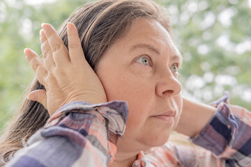 mature caucasian woman 50 years holding hand to sore ears, close up female face with facial...
