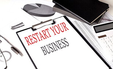 RESTART YOUR BUSINESS text on paper clipboard with chart and notebook on withe background