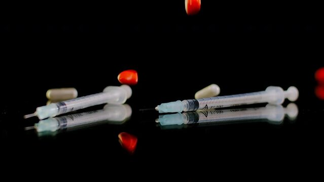 Two syringes on table with white and orange pills falling in slow motion at black background. Concept of drug trafficking