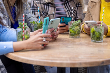 Amidst the vibrant ambiance of an urban cafe, a close-knit group of four multiracial women share drinks, laughter, and the warmth of friendship. Engrossed in their smartphones, their hands deftly