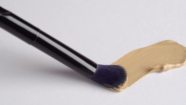 A smear of foundation cream or concealer with a brush on a white background, macro. Texture of cosmetic liquid foundation or beige cream smudge, smear, stroke. Advertising of professional cosmetics.