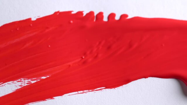 Close up of artist holding paint brush and drawing gouache painting. Painting red strokes on white canvas