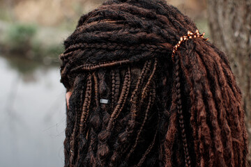 A girl with dark hair stands inquiringly at the camera. A walk in nature. The girl has many thin braids on her head