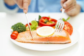 Asian elderly woman patient eating salmon stake and vegetable salad for healthy food in hospital.