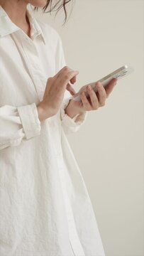 Woman in white shirt using mobile phone over white wall. Texting a message, surfing social media or browser concept