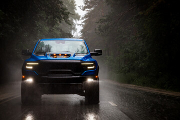 A blue new pickup truck is driving along a highway in the forest with a blurred background. Fast...