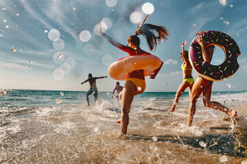 Old style photo of group of friends are having fun and running to sea beach with inflatable donuts - obrazy, fototapety, plakaty