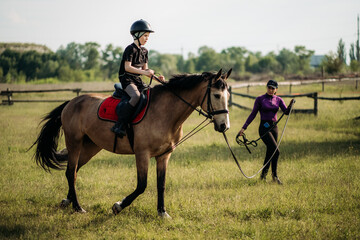 A teenage boy in a helmet learns horse riding in the summer, the instructor teaches the child...