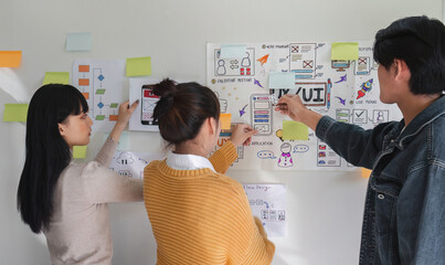 Image of a team of developers brainstorming UI and UX design ideas for a mobile app on a paper...