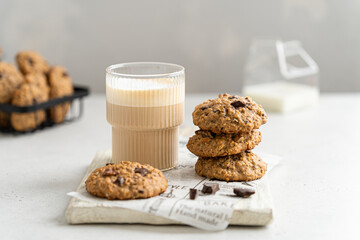 Stack of delicious freshly baked oatmeal cookies with nuts and chocolate drops and a glass of latte on a light background. Snack, breakfast concept. Healthy oat biscuits with chocolate recipe