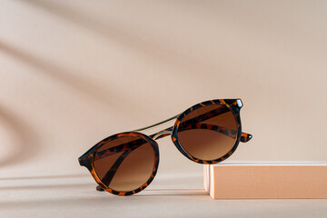 Womens Tortoiseshell frame sunglasses on a podium on a beige background with shadows. Trendy...