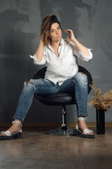 Confident woman in shirt, sandals and torn jeans straightening hair to side sitting with spread...