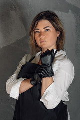 Portrait of confident lashmaker standing on gray background and putting on black medical glove, getting ready for work.