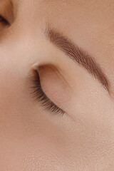 Close up of face of young caucasian woman with closed eyes, brown straight brow, black eyelashes and natural make-up.