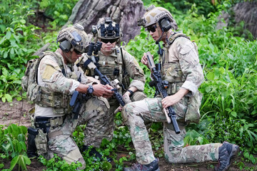 Fototapeta premium Military army soldiers tactical team, commando group moving cautiously in forest area, kneeling and looking around, covering comrades, controlling sectors. Commander showing halt or stop hand signal