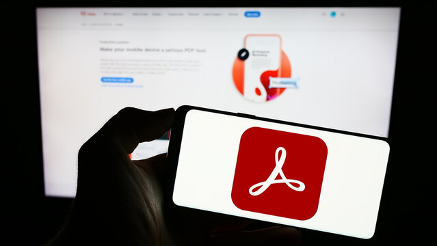 Stuttgart, Germany - 09-23-2023: Person holding cellphone with logo of PDF management software Adobe Acrobat on screen in front of business webpage. Focus on phone display.