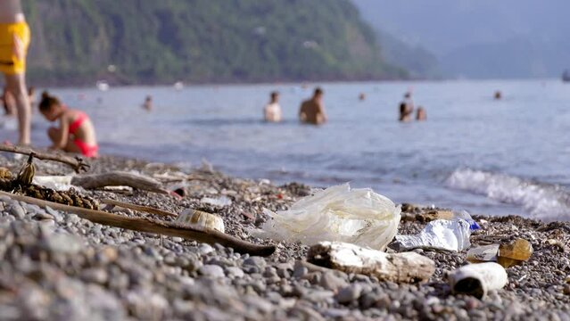 Ecology, plastic waste, environmental emergency and water pollution - concept of ecology. People swim in sea next to pile of garbage washed ashore or collected by volunteers;.