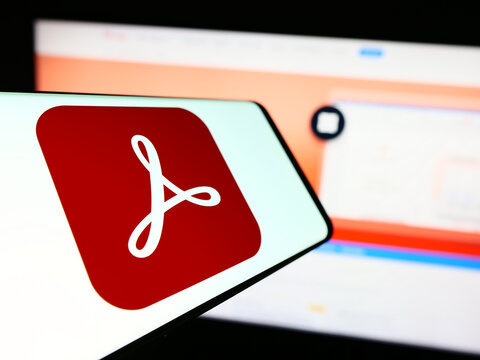 Stuttgart, Germany - 09-23-2023: Cellphone with logo of PDF management software Adobe Acrobat on screen in front of company website. Focus on center-left of phone display.