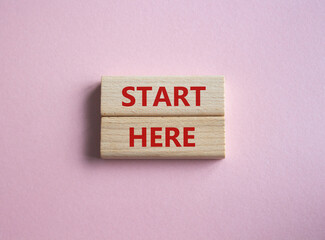 Start here symbol. Wooden blocks with words Start here Beautiful pink background. Business and...