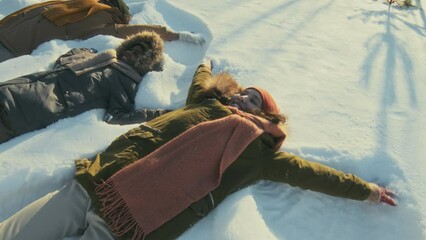 High angle view shot of cheerful ethnically diverse man, woman and their son lying on snowdrift making snow angels