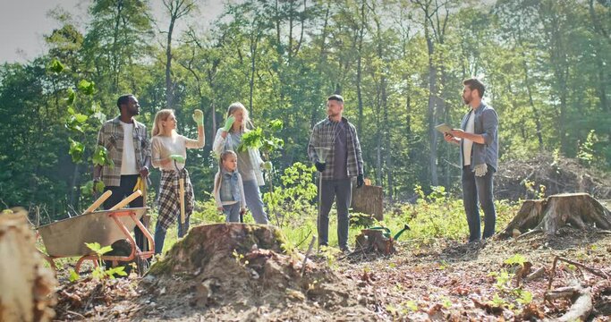 Group of happy people kids and adults listening to instructions from leader. Enthusiastic volunteers planting trees in forest. Environment activists providing forestation work. Nature concept.