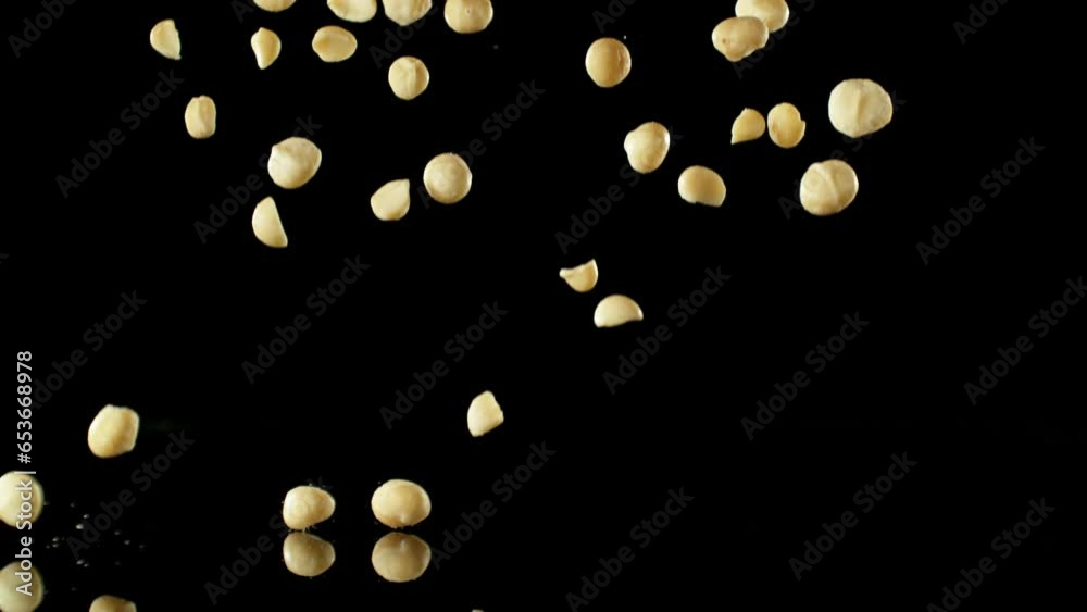 Poster super slow motion of falling macadams nuts with reflection. isolated on black background. filmed on 