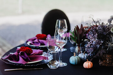 Festive Halloween table setting in black and purple colours with red roses, pumpkins and prickly plants.  