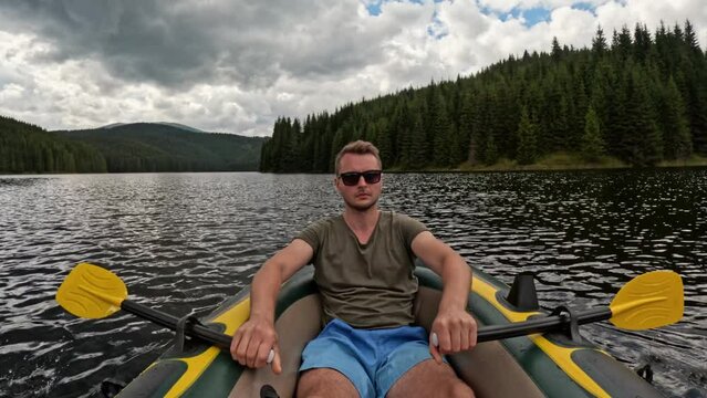 Fit man on a boat paddling with yellow paddle on a mountain lake. Healthy lifestyle recreation activity