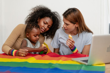 Multiethnic mother sit in living room having fun relaxing at home with her son and lesbian girlfriend. Happy biracial kid bonding with his LGBT family. Enjoyment and affection of diverse parenthood