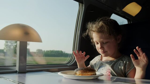 A child eats burger, sitting in a train compartment while traveling