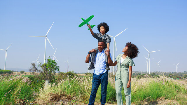 African American Happy Family, father mother, and child daughter sits on the shoulders of his father withholding airplane model on wind turbine farms, wind turbines, alternative renewable energy, - Powered by Adobe