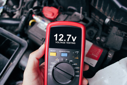 Car battery voltage testing with a digital multimeter by auto technician, Car voltage current display on black screen of digital multimeter, Car maintenance service concept