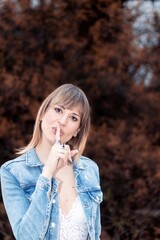 pretty woman in a denim jacket and a white lace top making the silence gesture