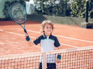 Positive kid raising racket while playing tennis on court