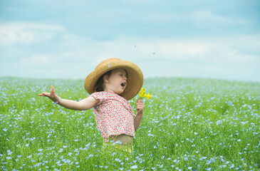 Adorable child singing in a straw hat with a bouquet of yellow flowers in the middle of a beautiful field of flowers. - 653707137
