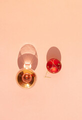 Minimal holiday concept  brandy glass and red Christmas ball on sunny day. Decoration and shadows on pink background. Flat lay.