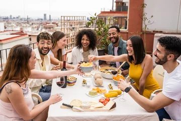 Fotobehang Cheerful group of diverse friends eating and drinking at a terrace table. Young and relaxed people having fun in a rooftop dinner party. © carlesiturbe