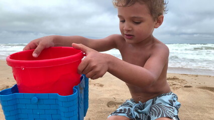 Cute infant boy playing at beach with buckets and water