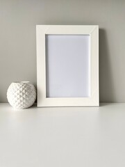 Blank photo frame mockup, white. Vase. Scandinavian interior design. Light background. Foreground. Copy space