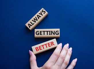 Always getting better symbol. Wooden blocks with words Always getting better. Beautiful deep blue background. Businessman hand. Business and Always getting better concept. Copy space.