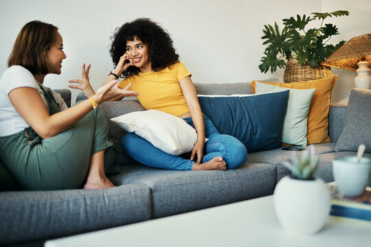 Women, friends and conversation in a home with gossip, discussion and happy in a living room. Couch, smile and people on a sofa with gossip or social together in a house lounge with speaking together