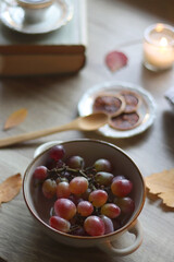 Cup of tea or coffee, plate with desserts, dried oranges, bowl of grapes, scented candles, vintage books, pumpkins and autumn leaves on the table. Autumnal hygge. Selective focus.