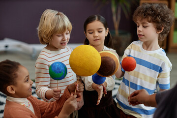 Diverse group of children holding planet models in preschool class and learning about space