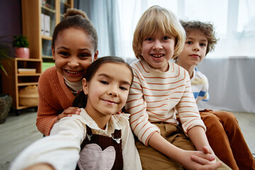 Diverse group of little children taking selfie photo and smiling at camera in preschool class or kindergarden