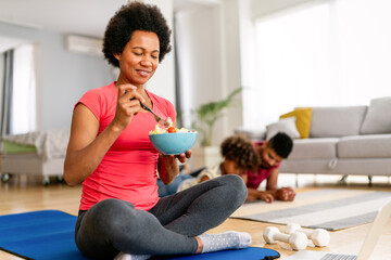 African american woman with family on background eating a healthy salad after workout. Fitness