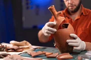 Male archaeologist working in the office late at night studying an ancient vase or vessel while...