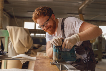 Professional carpenter cutting wood with an electric jigsaw machine in a carpentry workshop - obrazy, fototapety, plakaty