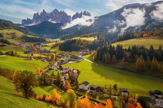 A captivating image of the quaint Santa Maddalena village nestled in the Funes valley of the Dolomite Alps, Italy. The serene mounting landscape is adorned with green fields and autumn-colored trees