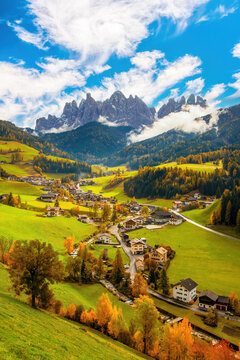 A captivating image of the quaint Santa Maddalena village nestled in the Funes valley of the Dolomite Alps, Italy. The serene mounting landscape is adorned with green fields and autumn-colored trees