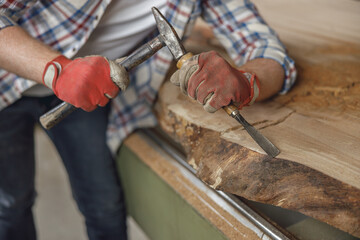 Close up of craftsman working with chisel while cutting wooden plank in carpentry workshop
